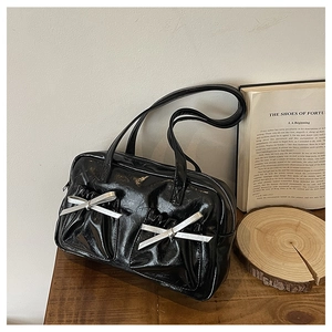 Close-up of black patent leather tote bag with silver bow details on a wooden table