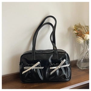 Detail of a black glossy shoulder bag with pleated pockets and silver bows on a desk