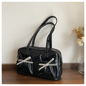 Close-up of black glossy patent leather tote with silver bows on a wooden table