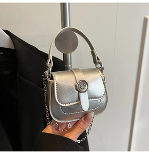 Detail of silver metallic mini bag featuring a circular metal buckle and chain strap