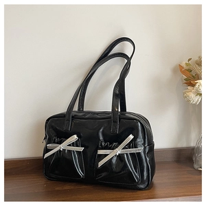Detail of black glossy tote bag featuring pleated pockets and silver bow accents