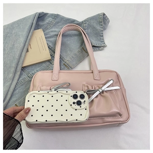 Detail of pink bow tote bag with polka dot phone case on white bedding scene