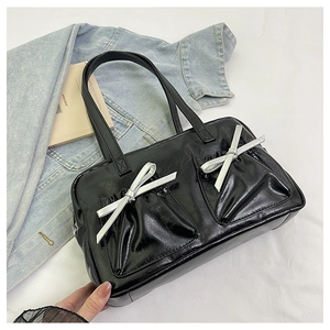 Detail of glossy black tote bag featuring twin front pockets and silver bow accents