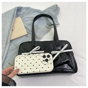 Close-up of black glossy leather tote bag with silver bow and polka dot phone case