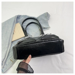 Detail of black pleated leather tote bag featuring a decorative silver metal bow charm
