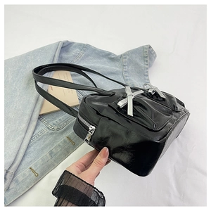 Close-up of black glossy leather tote bag with silver bows and metal zipper detail