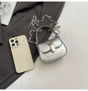 Mini silver metallic square bag with metal ring buckle and chain strap next to a phone