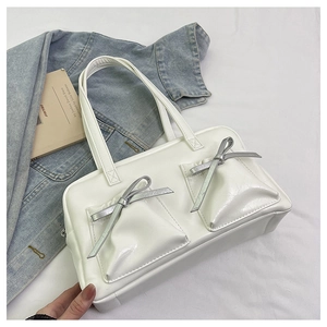 Detail of white glossy tote bag featuring two front pockets and silver bow accents