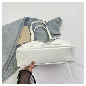 Detail of white leather tote bag featuring a side pocket with silver ribbon bow decor