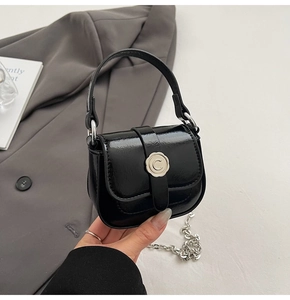 Detail of black patent leather mini bag featuring flower buckle and silver chain strap