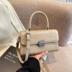 Sac carré crème minimaliste avec poignée et boucle argentée sur un canapé douillet