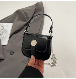 Detail of a mini black saddle bag with silver wax seal buckle and thin chain strap