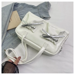 Close-up of white glossy tote bag with two silver metallic bow accents and zip closure