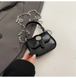 Detail of a mini black glossy shoulder bag with silver hardware and chain strap