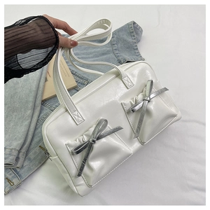Close-up of white tote bag featuring dual front pockets and silver bow decorations