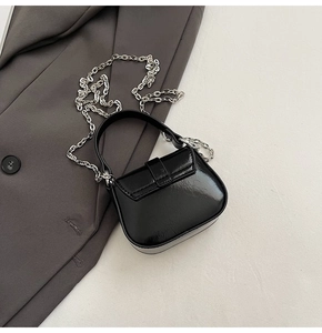 Close-up of black glossy patent leather mini bag with silver chain and textured finish