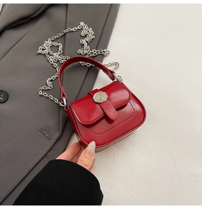 Detail of red patent leather mini crossbody bag featuring a silver embossed C-buckle closure