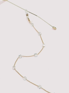 Close-up of golden metal eyewear chain with transparent square crystals on violet background