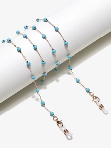 Detail of gold chain glasses strap with turquoise beads on white cylinder display