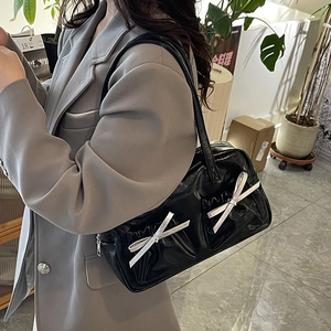 Glossy black bow tote bag with dual front pockets shown on shoulder in lifestyle scene