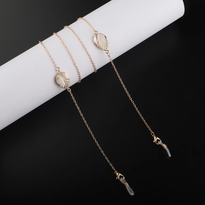 Golden eyewear chain with leaf shell pendants on a white cylinder stand over black background