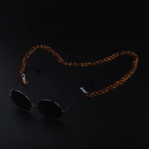 Detail of amber acrylic glasses chain attached to black sunglasses on dark background