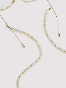 Detail of beaded eyewear chain with white pearls and gold metal spacers on pink background
