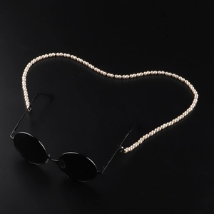 Retro black round sunglasses with elegant white faux pearl chain strap on a black surface