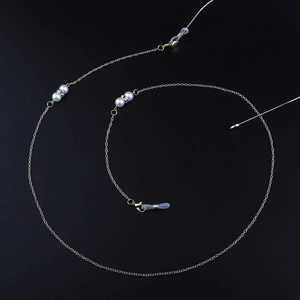 Dettaglio della catena per occhiali dorata con perle bianche, strass e passanti in gomma