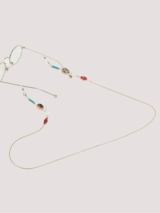Detail of golden glasses chain with shell charms and colorful beads on a pink background
