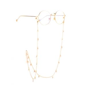 Détail d'une chaîne de lunettes dorée avec perles blanches sur des lunettes rondes