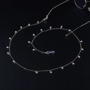 Détail de la chaîne de lunettes dorée avec perles blanches sur fond noir élégant