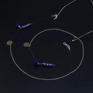 Détail de la chaîne de lunettes dorée avec pompons bleus et disques en filigrane