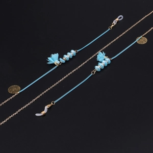 Détail de la chaîne à lunettes avec perles en verre bleues et pompons sur fond noir