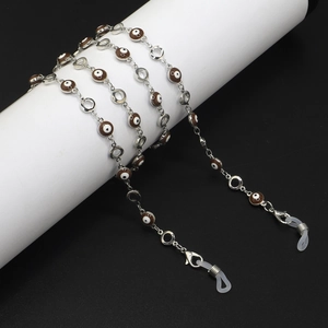 Detail of silver eyewear chain with brown evil eye charms on a white display stand