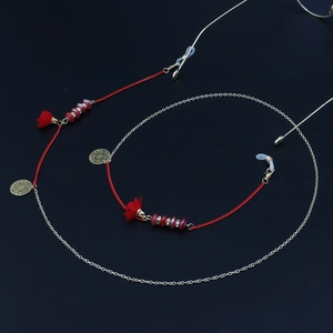Détail du gland rouge et de la chaîne de lunettes dorée avec perles sur fond noir mat