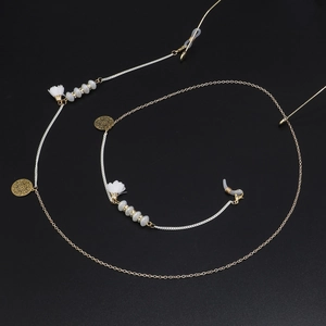 Détail de la chaîne à lunettes dorée avec perles blanches, pompons et pendentifs ajourés