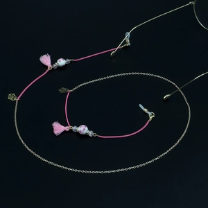 Detail of pink tassel eyeglass chain with ceramic beads and gold metal links on black