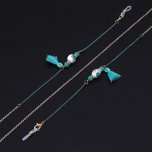 Detail of handmade ceramic beads and green tassels on a gold metal eyewear chain