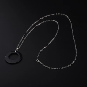 Silver chain necklace with a minimalist black circular pendant on a dark background