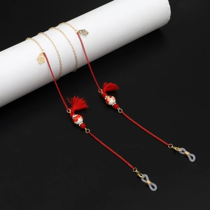 Detail of red tassel and ceramic bead on handcrafted eyeglass chain with gold metal accents