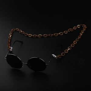 Detail of amber tortoiseshell acrylic eyewear chain attached to black round sunglasses