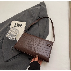 Top-down view of dark brown faux crocodile leather shoulder bag on a gray suit jacket