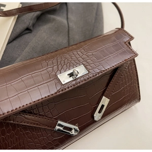Macro view of dark brown faux crocodile leather shoulder bag with silver turn-lock closure