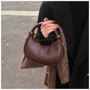 Close-up of a dark brown half-moon leather bag with minimalist knotted handle detail