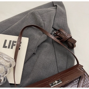 Detail of dark brown crocodile pattern leather handbag with silver metal buckle closure