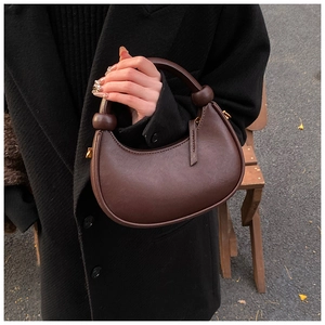 Detail of dark brown leather half-moon bag with decorative knots and golden hardware