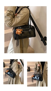 Detail of black glossy shoulder bag featuring retro buckle and brown teddy charm