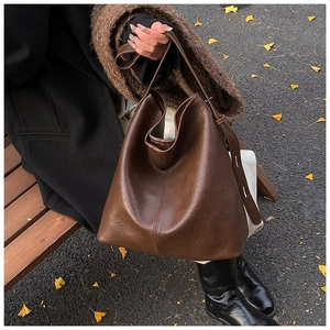 Brown leather tote bag with soft pleats and vertical stitching in an autumn park setting