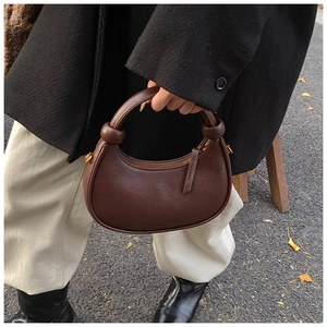 Detail of dark brown leather crescent bag with unique knot handle on asphalt background